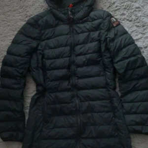 Svart dunjacka Parajumpers S - Säljer en svart, lång och superlätt dunjacka från Parajumpers i storlek S. Jackan har huva, dragkedja framtill och klassisk PJS-patch på ärmen. Perfekt för kalla dagar och riktigt snygg passform. Fylld med dun och fjäder för extra värme.