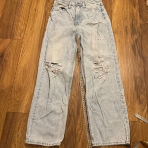 Ljusblåa raka jeans med slitningar - Säljer ett par ljusblå jeans med raka ben och snygga slitningar på både fram- och baksida. Jeansen har hög midja, klassisk femficksdesign och är tillverkade i denim. 