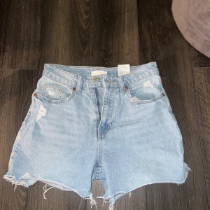 Ljusblå jeansshorts från H&M - Ljusblå jeansshorts från H&M i klassisk femficksmodell. Hög midja och råa, fransiga benslut för en avslappnad vibe. 