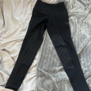 Svarta ridleggings från ZacZess XS - Svarta ridleggings från ZacZess i storlek XS. De har hög midja och mönstrade silikonpartier på insidan av benen för extra grepp. Snygg, tight passform och praktiska fickor på sidorna. Perfekta för ridning och träning. Ordenarie pris 1200