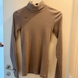 Beige ribbad polotröja från JJXX - Supersnygg beige polotröja från JJXX i ribbat material. Tröjan har lång ärm och en klassisk polokrage som ger en clean och stilren look. Perfekt att styla med jeans eller kjol för en enkel men trendig outfit.