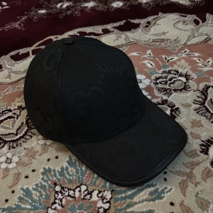 Svart keps med GG-mönster - Snygg svart keps med diskret GG-mönster över hela kepsen. Klassisk form med böjd skärm och strukturerad panel. Perfekt accessoar för att lyfta din outfit med en lyxig touch.
