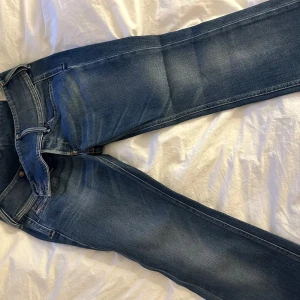 Diesel jeans  - Säljer ett par blå jeans med snygg tvätt och slitningar. Jeansen har hög midja, raka ben och råa, fransiga benslut för en cool look. Stängs med knappar framtill och har klassiska fickor. Perfekta för dig som gillar en avslappnad men trendig stil.