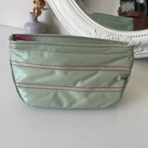 Mintgrön necessär från Clinique - Mintgrön necessär från Clinique i syntetmaterial med rosa dragkedja och dekorativa rosa sömmar. Perfekt storlek för smink eller småprylar, . Enkel och stilren design med mjuk form och praktisk öppning upptill.kan möta er i Stockholm city