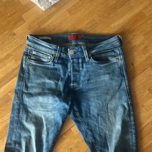 Blå slim fit jeans Jack & Jones 29-32 - Snygga blå jeans från Jack & Jones i modellen Slim/Glenn. Jeansen har klassisk femficksdesign, normalhög midja och smal passform. Tillverkade i stretchig denim för extra komfort. Perfekta för en stilren och avslappnad look.