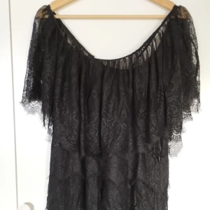 Svart spetsklänning offshoulder - Supersnygg svart kort klänning eller blus med möjlighet till offshoulder och vida ärmar i spets. Klänningen har en inner klänning och ett vackert spetsmönster över hela plagget. Perfekt för dig som vill sticka ut med en elegant och trendig look eller som önskar lite latin romantik. Säg till om du vill ha bild på hela varan; Bilderna beskärs så dumt i appen.