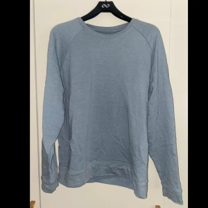 Ljusblå sweatshirt från ASOS - Enkel och stilren ljusblå sweatshirt från ASOS i storlek L. Tröjan har rund halsringning och långa ärmar, perfekt för en chill och avslappnad look. Tillverkad i mjuk bomull som känns skön mot huden.