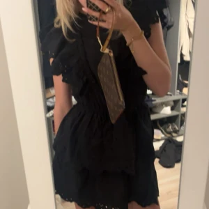 Svart volangklänning med broderi - Supersöt svart kortklänning med volanger och broderade detaljer. Klänningen har markerad midja, korta ärmar med volang och en luftig kjol. Perfekt för dig som gillar romantisk och trendig stil.