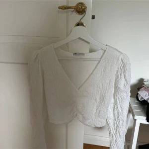 Vit topp - Supersöt vit croppad blus från Zara med v-ringning och lång ärm. Toppens tyg är lätt strukturerat och ger en lyxig känsla. Perfekt till jeans eller kjol för en fräsch look. Säljer då den inte kommer till användning längre!