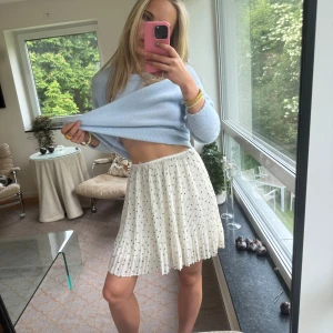 Plisserad vit prickig kjol från Samsøe Samsøe - Superfin plisserad kortkjol från Samsøe Samsøe i vitt med små mörkblå prickar. Kjolen har en lätt och flowy känsla, perfekt för varma dagar. Resår i midjan för skön passform och snyggt fall. Enkel att styla med både stickade tröjor och t-shirts.