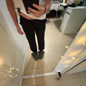 Svarta kostymbyxor från XOXO Friends - Svarta kostymbyxor från XOXO Friends i klassisk rak modell. Byxorna har hällor för bälte, knapp och dragkedja framtill. Snygg passform med raka ben och midja som sitter bekvämt. Perfekta för en clean och stilren look.