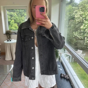 Svart grå  oversized jeansjacka - Säljer en svart jeansjacka i oversized modell med klassisk krage och silverfärgade knappar. Jackan har två bröstfickor med lock och raka sömmar som ger en clean look. Perfekt att slänga över en hoodie eller klänning för en chill vibe.