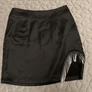 Svart kort satinkjol  - Säljer denna otroligt snygga satinkjolen från Bianca Ingrosso X Gina Tricot🤍 Svart satin med strass på sidan, storlek 36! Oanvänd men tagit bort lappen!