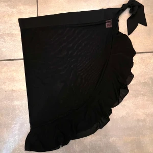 Pareo - Lägg till en touch av lekfull elegans till dina strandkläder. Tillverkad av mesh, denna pareo är perfekt för att lägga över din baddräkt. Med en volangdetalj längst ner.