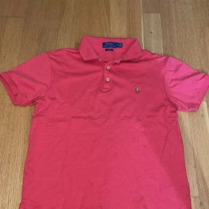 Rosa pikétröja Polo Ralph Lauren M - Snygg rosa pikétröja från Polo Ralph Lauren i slim fit-modell. Klassisk krage, två knappar och broderad logga på bröstet. Perfekt för dig som gillar stilrena och sportiga vibes. Tillverkad i mjuk bomull som känns skön mot huden.