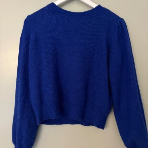 Blå stickad tröja med lång ärm - En enkel och snygg blå stickad tröja med rund hals och långa ärmar. Tröjan har en rak passform och ribbade muddar vid ärmslut och nederkant. Perfekt att slänga på sig när det är kyligt ute.