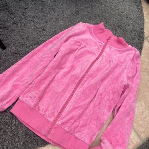 Rosa velourjacka str 134 - Säljer en supermjuk rosa velourjacka från Queen of Hearts med dragkedja framtill och ribbade muddar. Jackan har broderad logga vid höften och en klassisk sportig look. Perfekt för dig som gillar comfy och färgglada plagg.