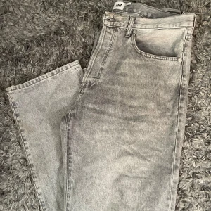 Grå jeans från 157, straight fit - Säljer ett par grå jeans från 157 i rak modell. Jeansen har klassisk femficksdesign, hög midja och råa, slitna benslut. 