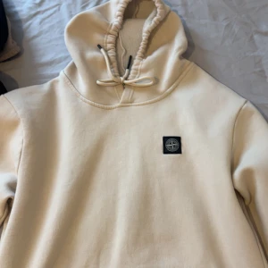 Beige hoodie från Stone Island  - Snygg beige hoodie från Stone Island i storlek XXL. Tröjan har huva med snörning och klassisk logopatch på bröstet. Mjuk insida och relaxed fit gör den perfekt för chill dagar. Passar dig som gillar stilrena och exklusiva streetwear-plagg.