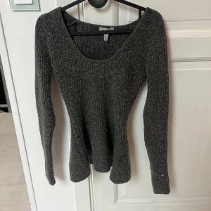 Mörkgrå ribbad stickad tröja H&M - Mysig mörkgrå stickad tröja från H&M med ribbad struktur och rundad, lite djupare halsringning. Långärmad och figurnära passform som sitter snyggt på kroppen. Perfekt för lager-på-lager under kyliga dagar.