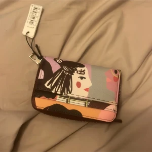 Färgglad plånbok med konstnärligt tryck - Plånbok i syntetmaterial med unikt konstnärligt motiv i rosa, lila, brun, grå och beige toner. Praktisk dragkedja runtom och flera fack för kort och mynt. Perfekt accessoar för dig som gillar färg och kreativ design.