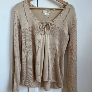 Beige stickad blus med snörning - Supersöt beige stickad blus från Odd Molly med lång ärm, v-ringning och snörning framtill. Blusen har fina hålstickade detaljer och lätt utsvängd passform. Perfekt för dig som gillar en romantisk och bohemisk stil. 💕