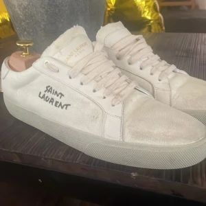 Saint laurent skor - Snygga vita sneakers från Saint Laurent i canvas med handskriven logga på sidan. Skorna har rund tå, platt sula och klassisk snörning. Perfekta för dig som gillar stilrena och exklusiva sneakers med en unik touch.