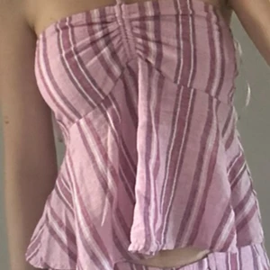 Randig rosa linnetopp från Bershka - Superfin randig linnetopp från Bershka i olika nyanser av rosa och vitt. Toppen är ärmlös med bandeau-modell, smockad rygg och tunna axelband som knyts i nacken. Luftig och flowy passform, perfekt för varma dagar. Har sytt där bak. Använd vid 2 tillfällen. 