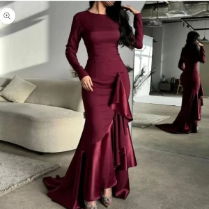Vinröd långklänning i satin med volang - Supersnygg vinröd långklänning i glansig satin med långa ärmar och figurnära passform. Klänningen har volangdetaljer framtill och en elegant släp. Den är köpt för 1800kr men har inte använts någon gång då den kom försent. Köpt från little lala boutique 