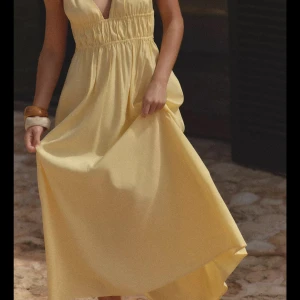 Ljusgul långklänning med smala axelband - Superfin ljusgul långklänning med smala axelband och v-ringning. Klänningen har resår i midjan för en snygg passform och ett luftigt, flowy fall. Perfekt för varma dagar och somriga vibes. Materialet känns lätt och bekvämt mot huden.