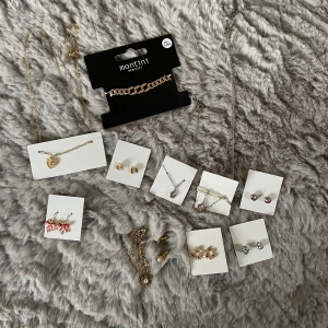 Mix av örhängen, halsband & armband - Stort smyckeskit med flera par örhängen, halsband och armband i både guld- och silverfärg. Inkluderar rosa stenar, hjärtformade detaljer, glittriga örhängen, röda rosettörhängen och ett chunky guldarmband från Montini. Alla smycken förutom det guldiga armbandet kommer från guldfynd julkalender ett tidigare år. 