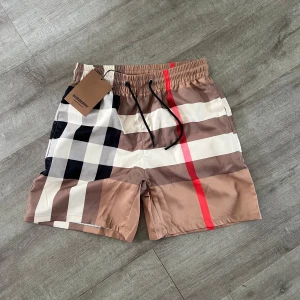 Rutig Burberry shorts med snörning - Snygga shorts från Burberry med klassiskt rutigt mönster i beige, svart, vitt och rött. Perfekta för sommaren och ger en lyxig vibe till din outfit. Priset är inte hugget i sten.