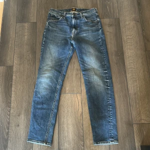 Blå jeans från Lee med straight fit - Snygga blå jeans från Lee med klassisk femficksdesign och raka ben. Jeansen har en lätt fade look med slitningar på låren och knäna. Perfekta för dig som gillar en tidlös och avslappnad stil.