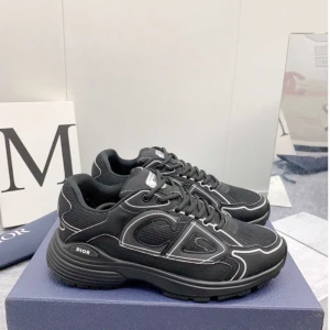Svarta Dior sneakers med vita detaljer - Snygga svarta Dior sneakers med vita kontrastsömmar och CD-logga på sidan och hälen. Skorna har en chunky sula, mesh och syntetmaterial samt snörning framtill. Perfekta för dig som vill ha en exklusiv och trendig look.