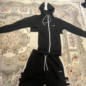 Hugo Boss Tracksuit / dress - Jätte fin Svart och vit Hugo boss tränings dress Zip up hoodien/koftan är i storlek S medans byxorna är i storlek M, men tracksuiten sitter bra för någon med storlek S Skicket på den är mycket bra, endast nopprig, ena ändan på snöret har ramlat av och loggan på baksidan av koftan har tappt lite, inget man märker av så länge man inte kollar jätte noggrant  Skicka meddelande vid några funderingar  Kolla gärna även in mina andra annonser