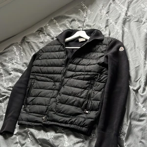 Svart Moncler cardigan  - Säljer en svart Moncler cardigan perfekt nu till sommarkvällarna. Jackan är i ett exstremt bra skick 9/10, ja Självklart är jackan äkta scann finns och  på sista bilderna. Det är storlek M men sitter mera som S! Perfekt till dig som vill ha en stilren och sticka ut nfc scannen funkar även med! Hör av dig om flera bilder eller andra funderingar!🤩🙌🏻👍🏻