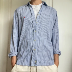 Blårandig skjorta från Morris - Snygg blårandig skjorta från Morris med klassisk krage och knäppning framtill. Skjortan är i bomull och har långa ärmar som enkelt kan rullas upp. Perfekt för dig som gillar en avslappnad men stilren look.