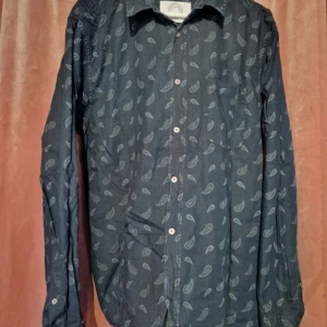 Mörkblå skjorta med paisleymönster - Snygg mörkblå skjorta från Contemporary med paisleymönster i ljusare nyans. Skjortan har klassisk krage, bröstficka och knäppning framtill. Perfekt för dig som vill sticka ut lite extra med ett coolt mönster.