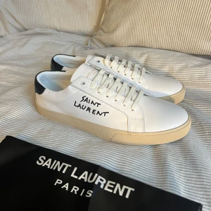 Saint Laurent skor (NYA) - Snygga vita sneakers från Saint Laurent i skinn med svart häl och handskriven logga på sidan. Klassisk rund tå, vita snören och beige sula. Perfekta för dig som gillar stilrena och exklusiva skor med streetkänsla. Obs 1nte 0rglnal