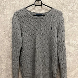 Grå kabelstickad tröja Polo Ralph Lauren - Kabelstickad grå tröja från Polo Ralph Lauren storlek L i barnstorlek sitter som xs i vanlig storlek med rund halsringning och diskret broderad logga på bröstet. Långärmad modell i mjuk bomull, perfekt för lager-på-lager och chill stil. Klassisk och tidlös design som funkar till allt.