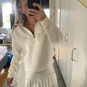 Vit half zip sweatshirt - Vit sweatshirt med half zip och hög krage. Tröjan har en avslappnad passform och är långärmad med breda muddar vid ärmslut och midja. Perfekt för en chill och enkel look. Materialet känns mjukt och bekvämt, troligen bomull eller en bomullsblandning.