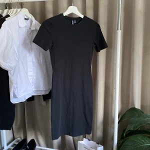 Svart tight kortklänning  - En svart, ribbad kortklänning från Pieces i storlek XS. Klänningen har korta ärmar, rund halsringning och en tight och figurnära passform. 