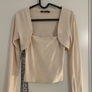 Beige bolerotopp från Gina Tricot - Beige bolerotopp med lång ärm och croppad bolerodetalj från Gina Trivot i storlek XS. Toppen har fyrkantig ringning och själva boleron sitter fast med toppen. Aldrig använd. 
