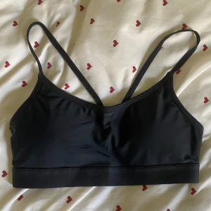 Svart topp - Svart bikiniöverdel från SOC med smala axelband som korsas i ryggen. Toppen är i stretchigt material och har en sportig look, perfekt för träning eller chill också! Enkel och stilren design utan mönster, med bred resår nedtill för extra stöd😻Den har removeable pads inuti💕Står strl S, men passar nog XS även. Använd 1 gång tror jag!
