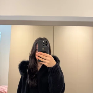 Populär svart jacka med pälsdetaljer - Snygg svart jacka med dragkedja och fluffiga pälsdetaljer på kragen. Aldrig använd.