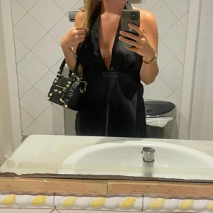 Svart kortklänning med djup urringning - Snygg svart kortklänning med djup v-ringad urringning och öppen rygg. Perfekt för en utekväll eller fest. Klänningen har en elegant passform och knyts i nacken.