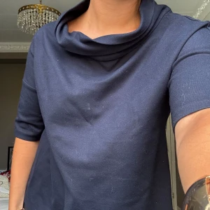 Mörkblå topp med trekvartsärm - Säljer en stilren mörkblå topp med trekvartsärm och en elegant draperad krage. Perfekt för en chic och avslappnad look. Passar bra till både jeans och kjol. 