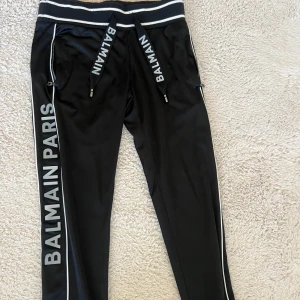 Svart hoodie från Balmain - Snygg svart hoodie från Balmain med dragkedja och vita detaljer. Den har en stor huva och långa ärmar. Perfekt för en stilren och sportig look.  PRISET KAN DISKUTERAS!!