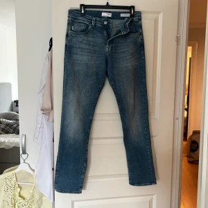 Blå jeans från Selected Homme - Säljer ett par snygga blå jeans från Selected Homme, modell Straight Scott. De har en klassisk straight passform med dragkedja och knapp. Perfekta för en stilren look.