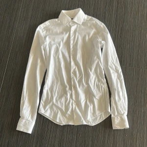 Vit skjorta från Dressmann - Säljer en stilren vit skjorta från Dressmann i extra slim fit. Skjortan är tillverkad i premium bomull med stretch och har långa ärmar samt knappar framtill. Perfekt för en elegant look. Pris kan diskuteras. 